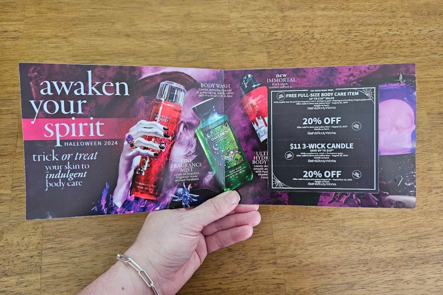 hand holding an open bath and body works halloween mailer with coupons