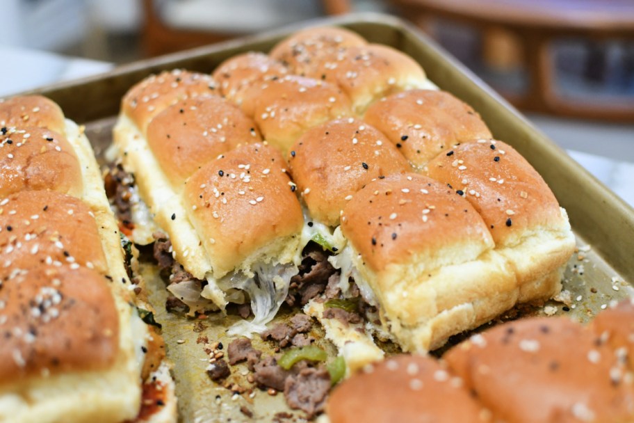 philliy cheesesteak hawaiian roll sandwiches on a sheet pan with cheese 