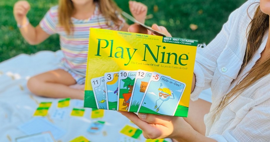 woman holding a Play Nine Card Game box, little girl in the background excited to play