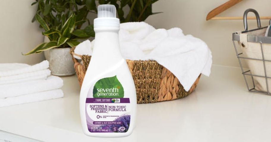 Seventh Generation Liquid Fabric Softener 32oz in Fresh Lavender bottle on laundry counter in front of laundry basket with white towels in it