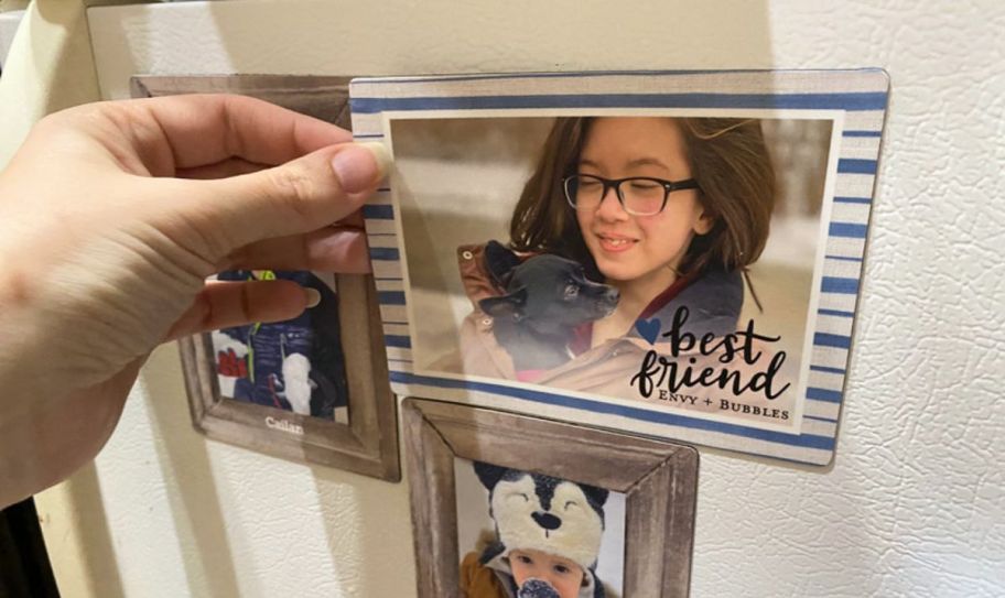 a womans hand place a photo magnet on a fridge.