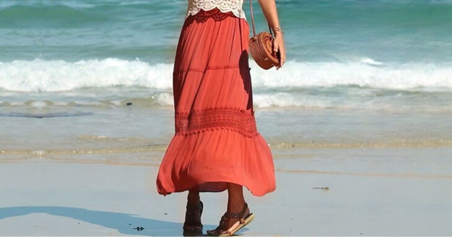 woman wearing MEROKEETY Women's Boho Elastic High Waist Pleated A-line Ruffle Lace Trim Tiered Midi Maxi Skirt with Pockets in caramel walking on beach