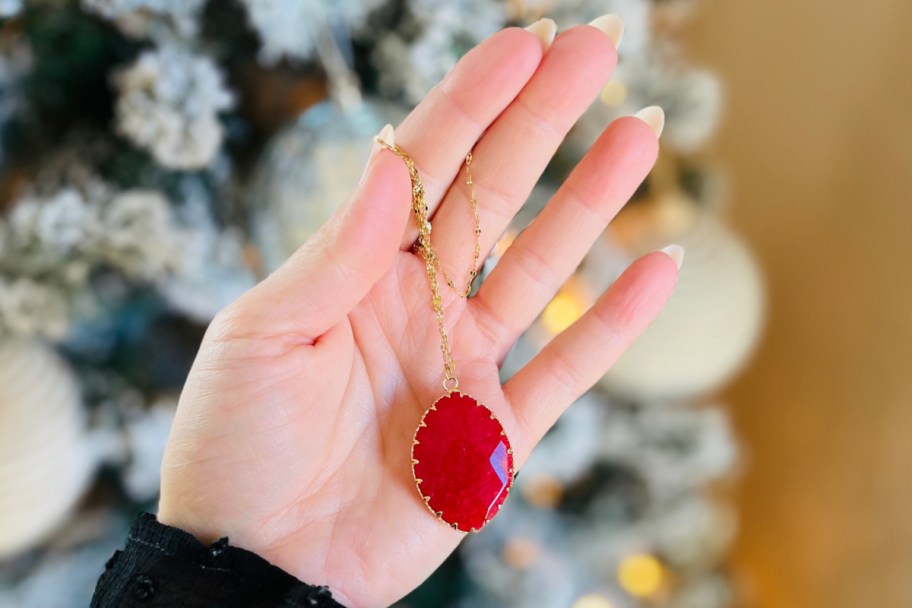 hand holding red ruby pendant necklace near tree