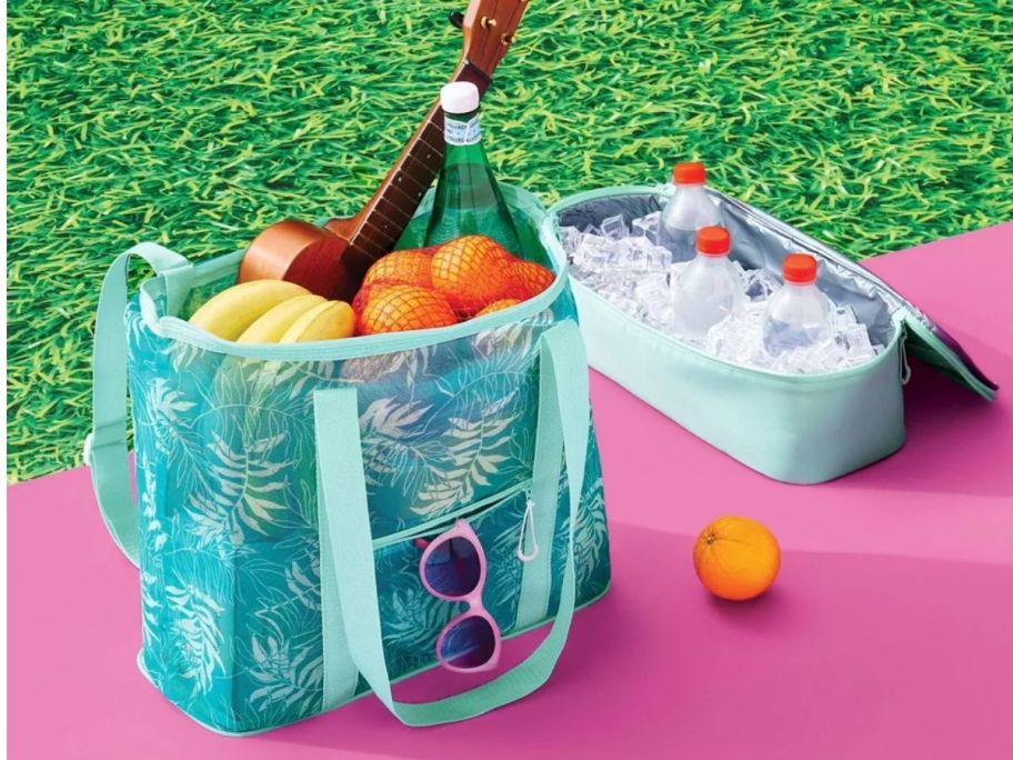 green palm tree print mesh tote bag next to it's detachable cooler that has ice and soda cans in it