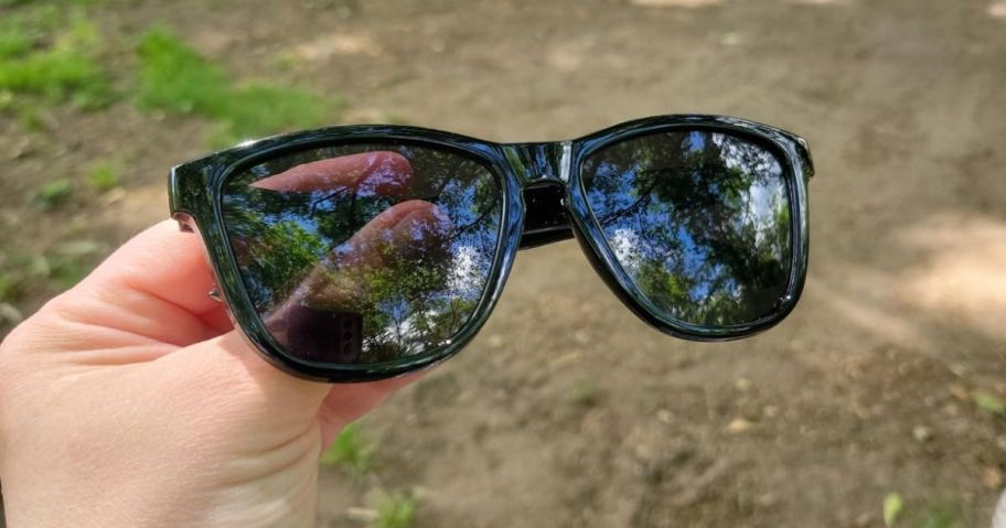 hand holding a pair Women's black Mirrored Sunglasses outside