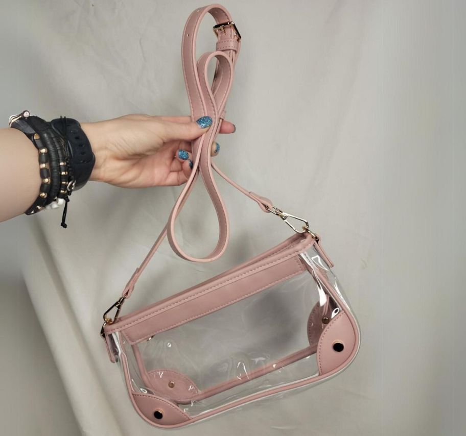 a womans hand holding a clear crossbody bag with pink PU trim