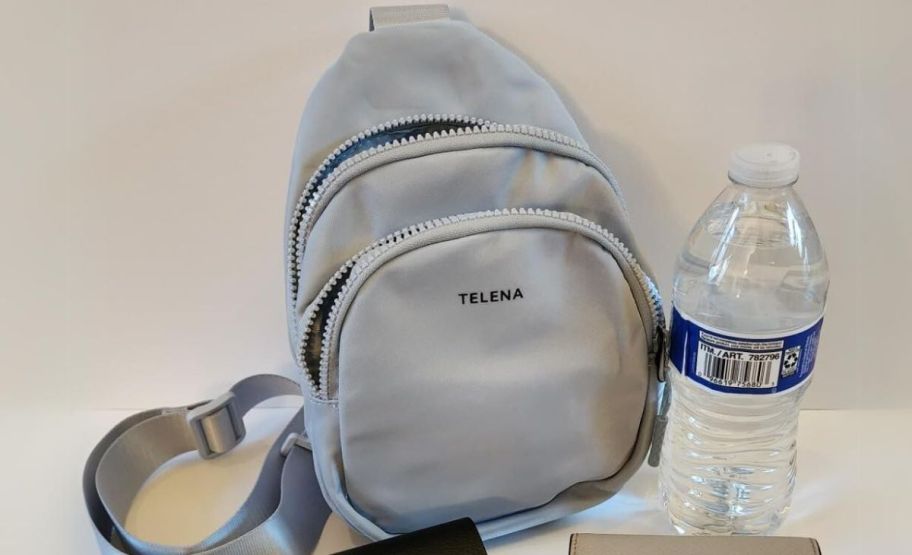 a gray sling bag next to a bottle of water