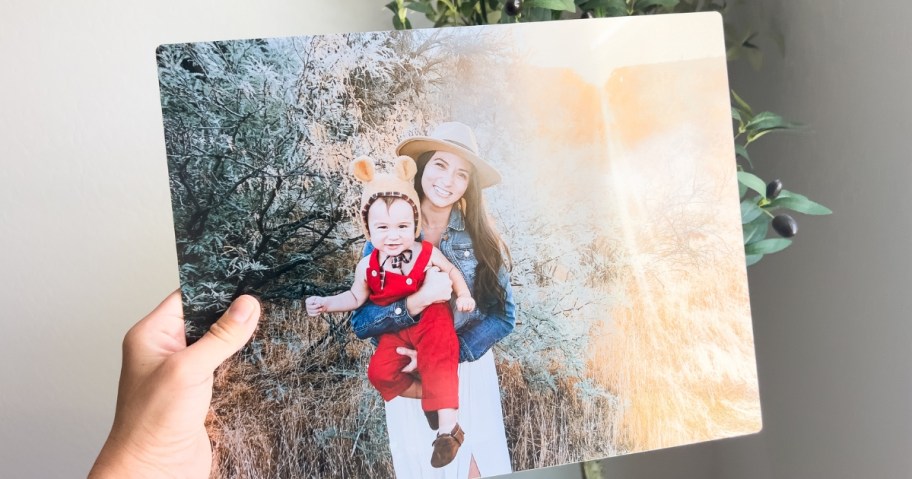 hand holding a large metal photo print of a woman holding her child