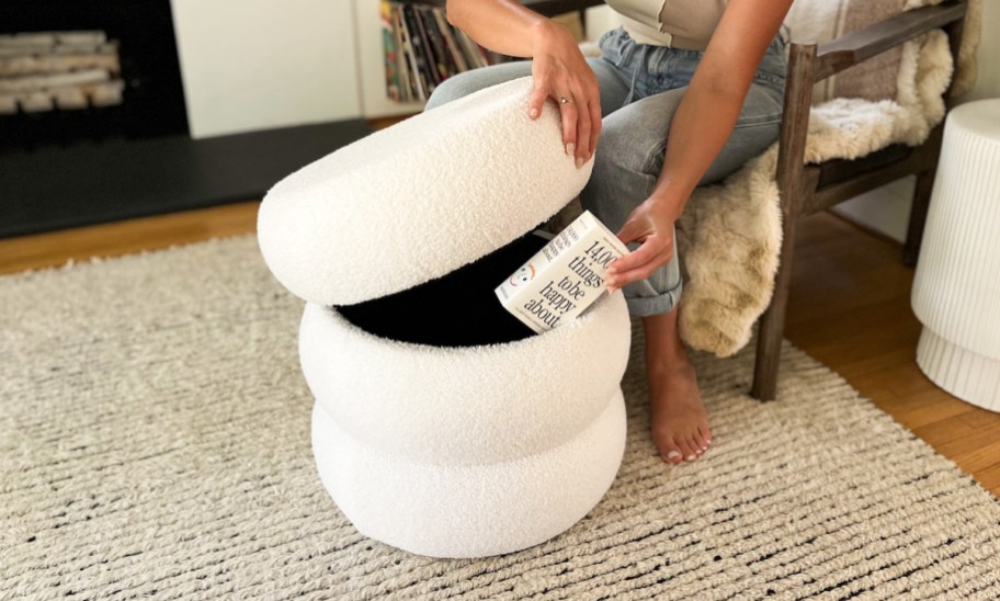 woman putting book inside of white boucle storage ottoman