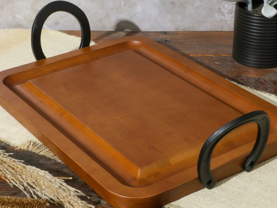 wood serving tray with black metal handles on a counter