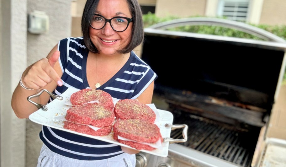 woman holding a plate of burger patties by the grill