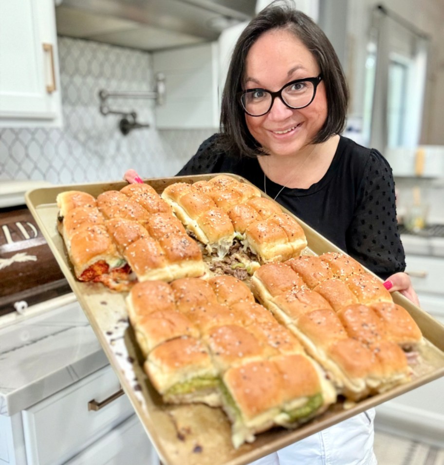 woman holding sheet pan with 4 slider sandwiches