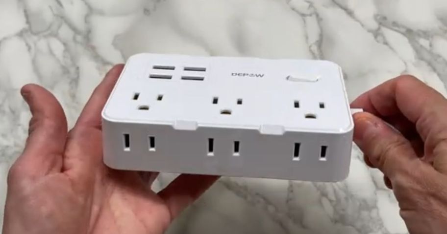 hand holding a small white power strip charging station, marble countertop behind it