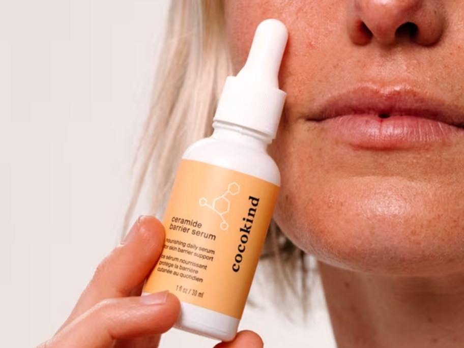 woman holding a bottle of Cocokind Ceramide Barrier Nourishing Daily Serum against her face