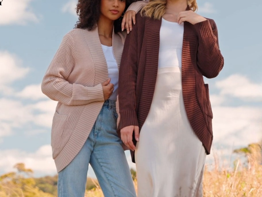 women wearing chunky knit cardigans - 1 in a pink color and 1 in a brown color