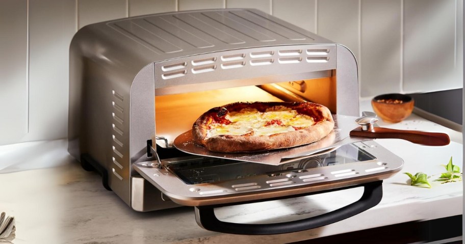 a stainless steel indoor pizza oven with a fresh baked pizza being pulled out of it