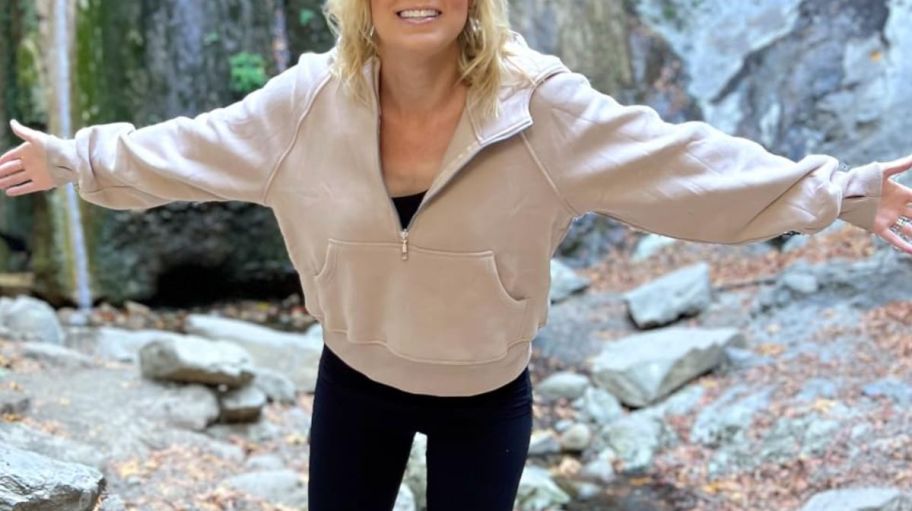a woman in a khaki half zip hoodie outdoors on a hiking trail