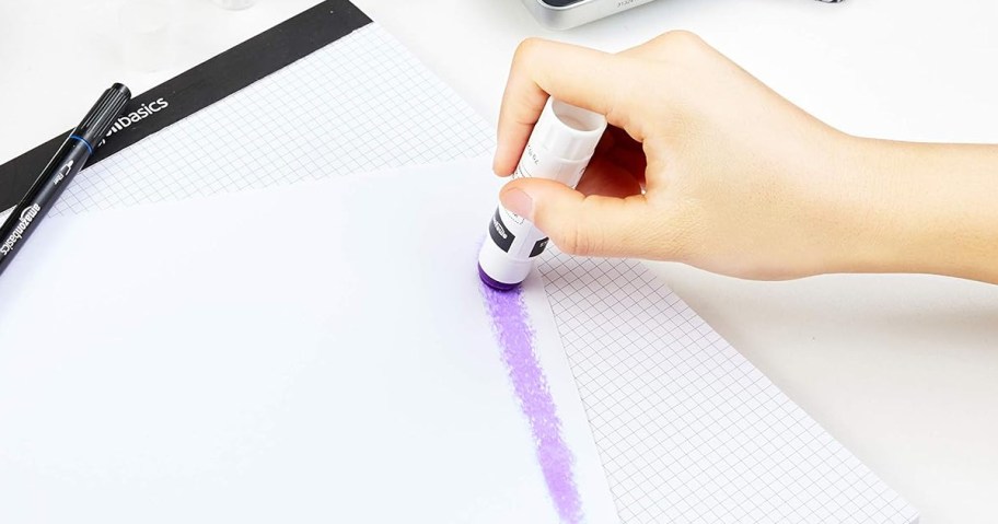 person using purple glue stick on white paper