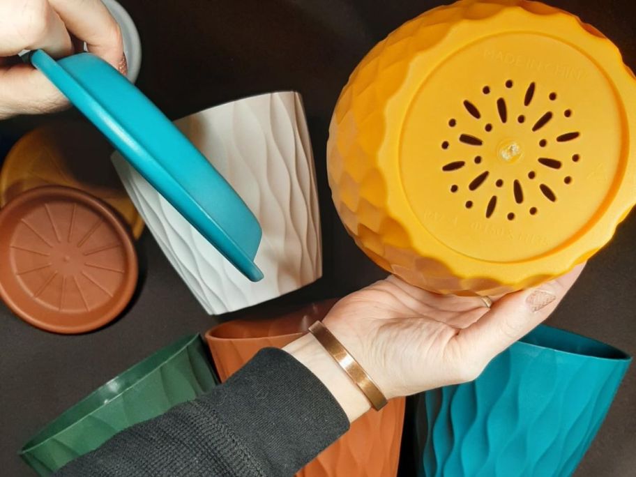 Hand holding a planter upside-down to show the drainage holes while holding the removable tray for catching excess water in the other