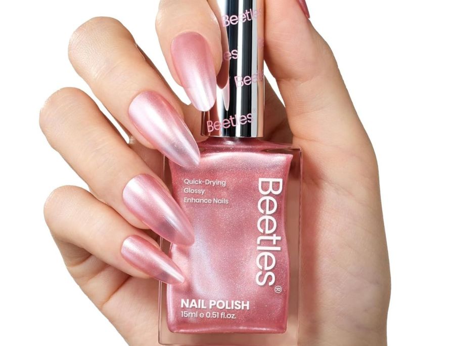 Hand holding a bottle of Beetles Nail Polish in a pearlized pink shade