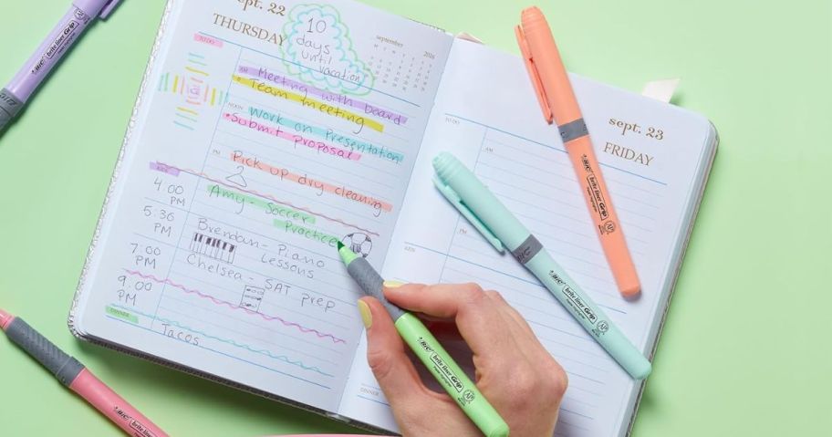 Hand using Bic Pastel highlighters to write in a planner