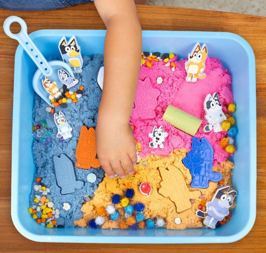 a little kid's hand playing with a Bluey family sensory bin