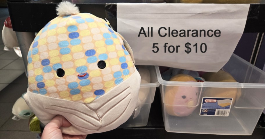 hand holding up squishmallow next to clearance sign
