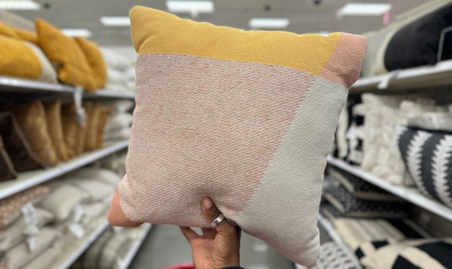 a womans hand holding up a color blocked throw pillow