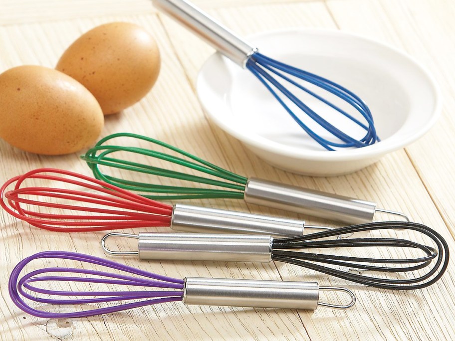 mini silicone whisks in various colors near bowl and eggs
