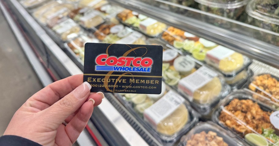 hand holding a black Costco Executive Membership card in front of the pre-made meals section