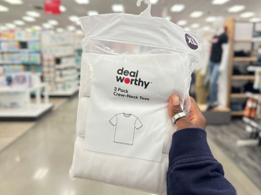 Hand holding up a pack of Dealworthy men's white tees at Target