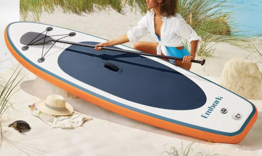 a woman on a beach with an inflatable paddle board.