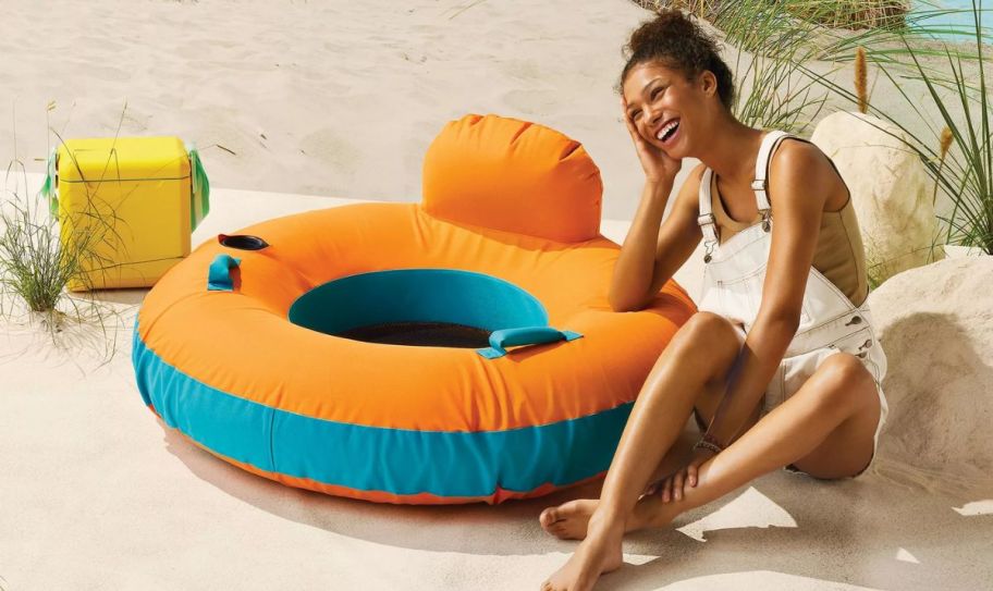 a model on a beach with an orange and teal round pool float