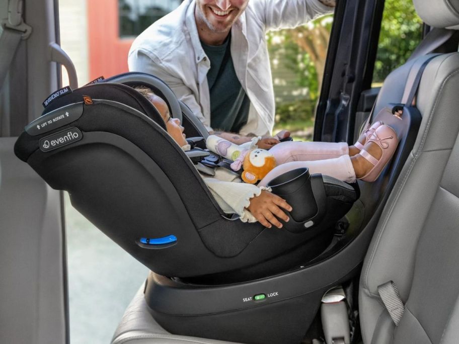 Baby sitting in the Evenflo Revolve360 Slim 2-in-1 Rotational Car Seat with dad standing outside of the open car door