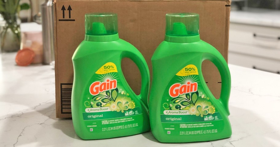 two green bottles of gain laundry detergent in front of shipping box