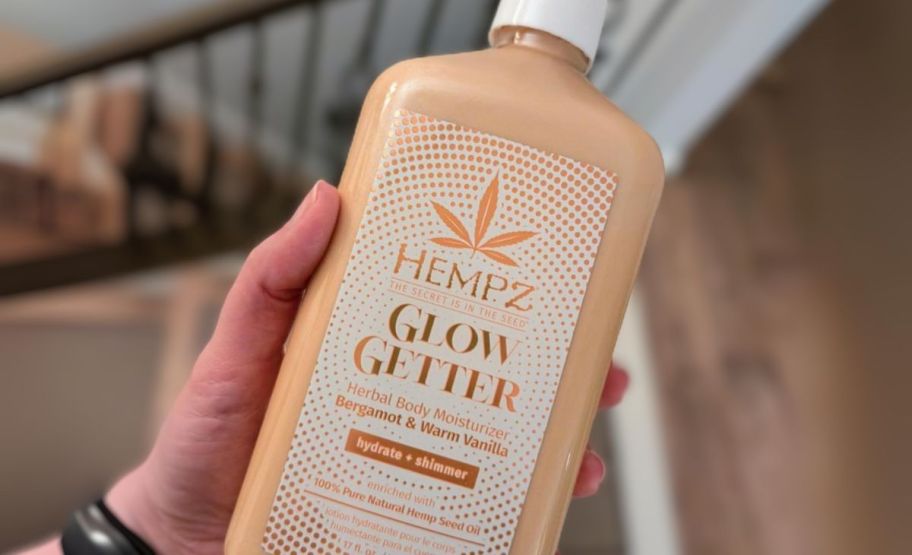 a womans hand holding a bottle of hempz shimmer lotion