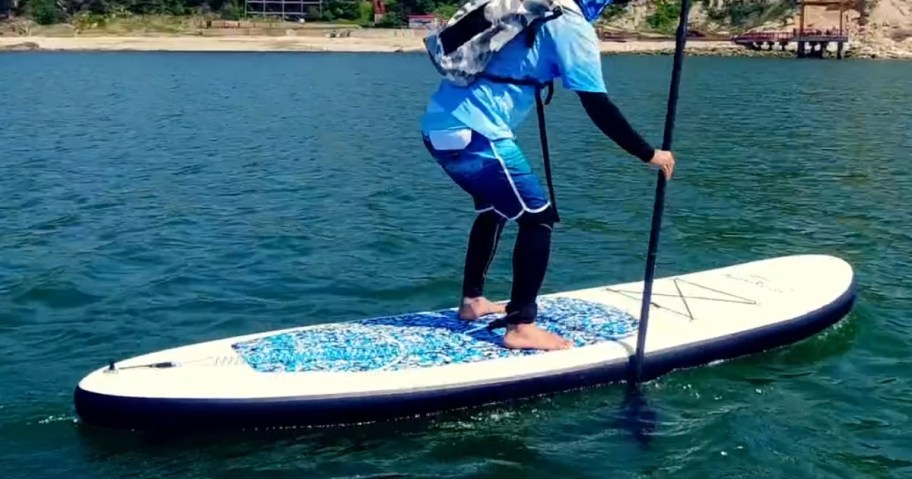 man standing on a white and blue inflatable paddle board, paddling thru the water