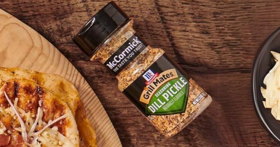 bottle of McCormick Grill Mates Dill Pickle Seasoning next to a pizza on a board and a bowl of cheese