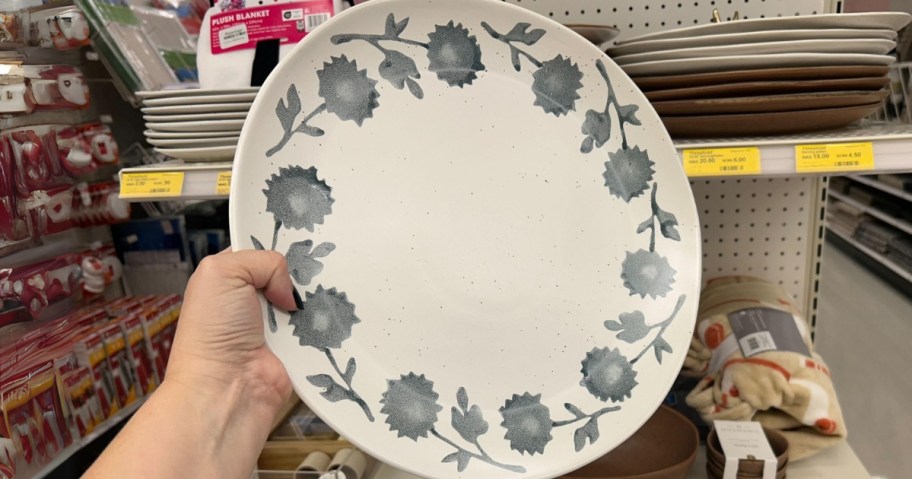 hand holding a large serving plate that's white with blue flowers around the boarder, store shelf with more plates behind it