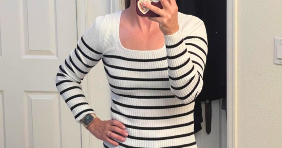 woman taking a selfie in a mirror wearing a white ribbed knit sweater top with black stripes