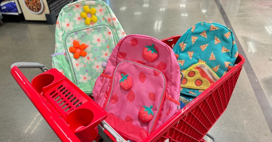 Target shopping cart with kid's backpacks in it with strawberry, flower and pizza designs on them