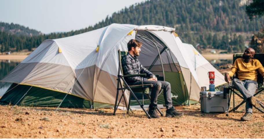 2 men sitting in camping chairs outside of a large 8 person dome 2 room tent in the outdoors