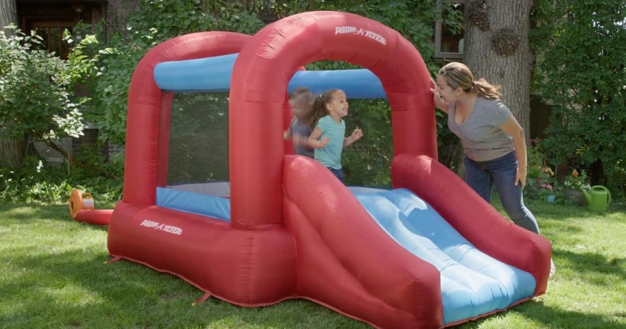 bright red and blue Radio Flyer kid's bounce house in a backyard kid playing inside and mom watching