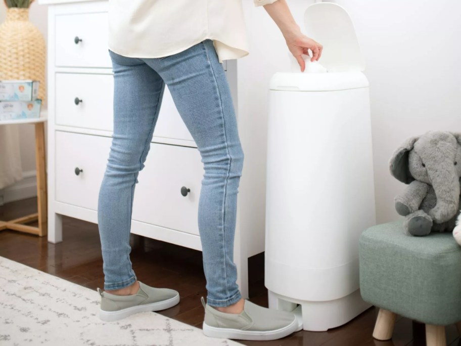 woman putting a diaper into a white Diaper Genie pail in a baby's nursery