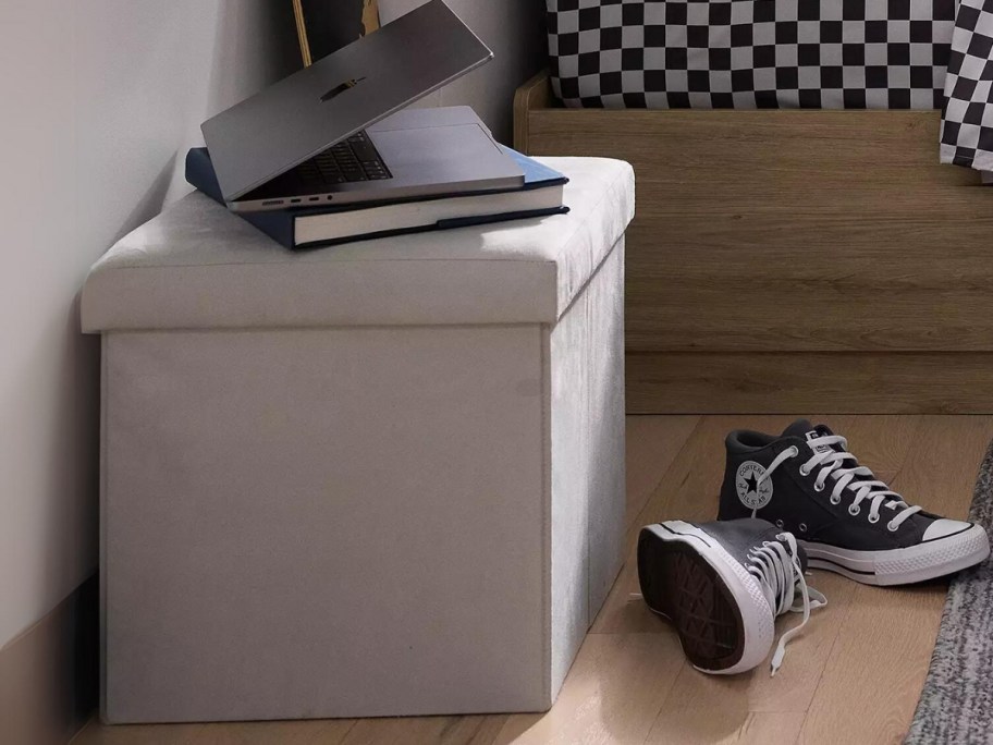 grey storage cube in a dorm room with books on it, Converse shoes in the floor next to it