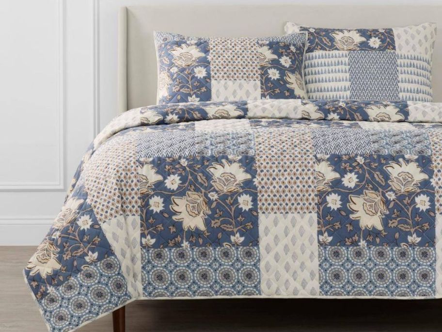 A bed with a blue, floral patchwork comforter