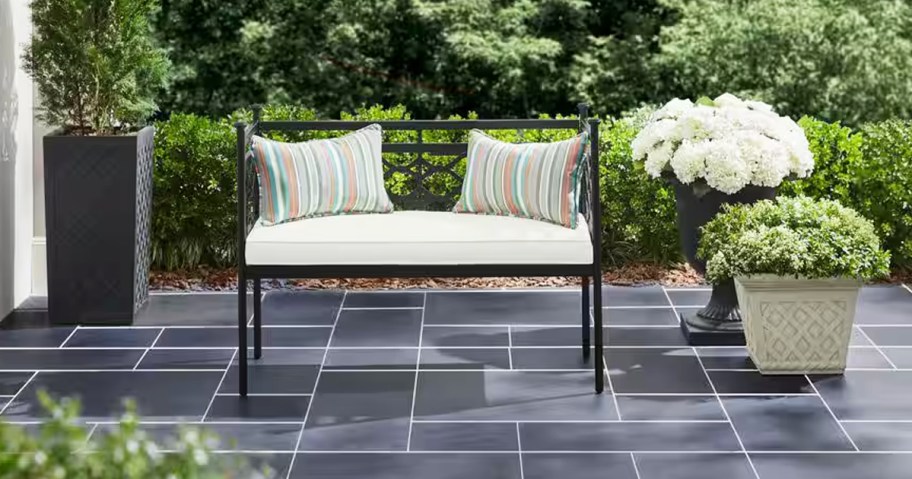 black metal outdoor bench with white cushions and striped throw pillows