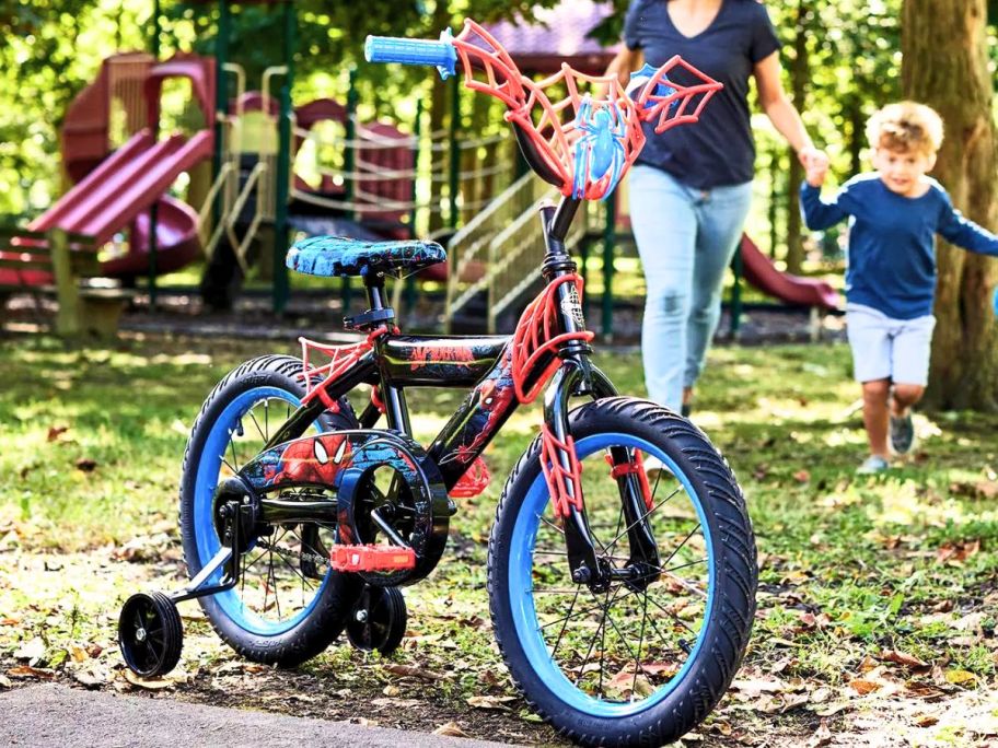 a blue and black spiderman kids bike with training wheels on a playground