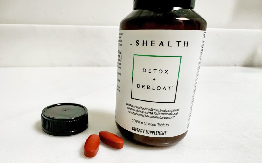 bottle of jshealth detox and debloat supplements with two pills sitting next to it on a counter