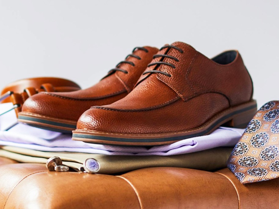 brown dress shoes sitting on top of folded clothes